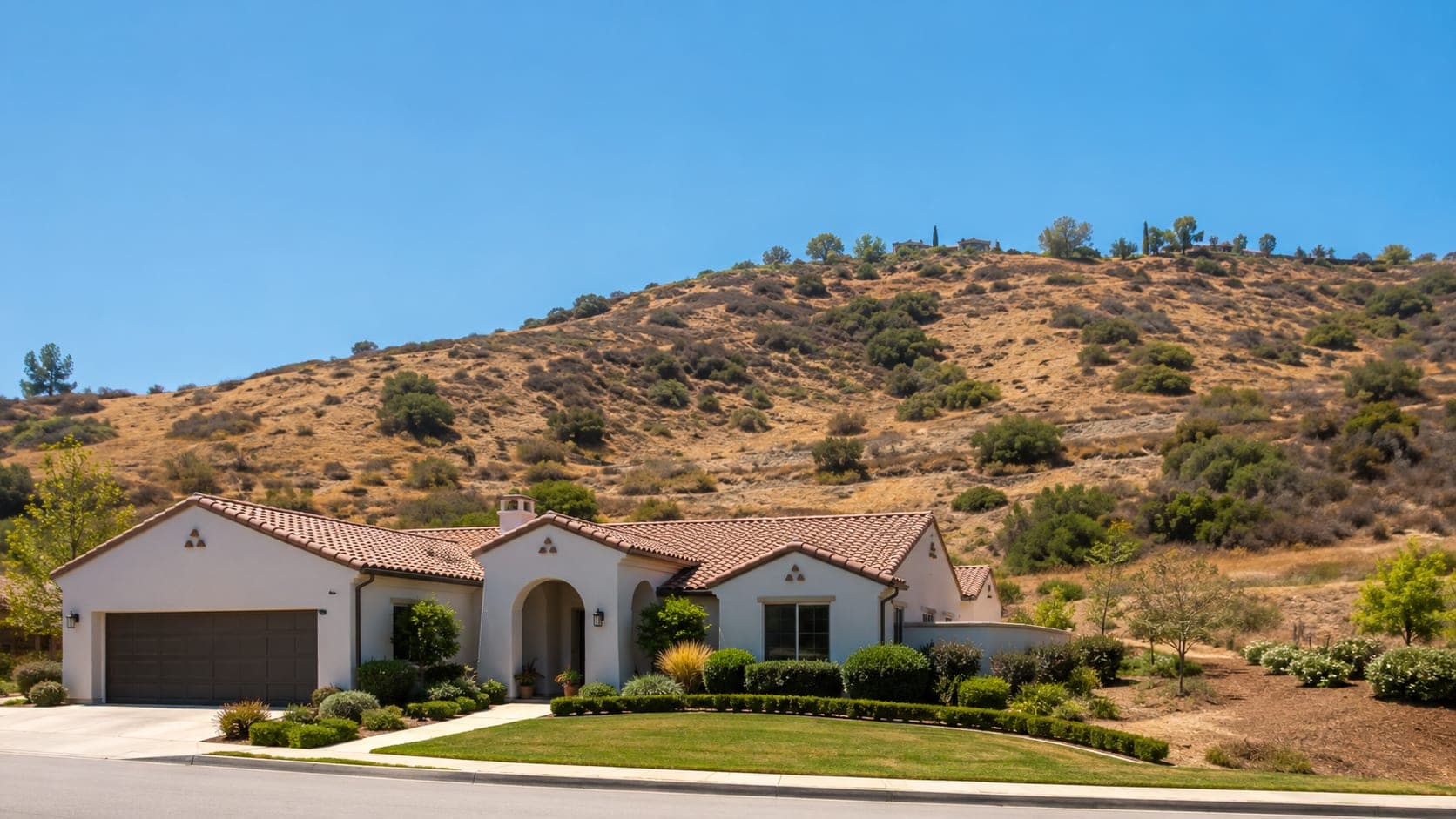 A tile-roofed Porter Ranch home on a landscaped lot at the foot of dry, brush-covered hills — the wildland-urban interface where LAFD brush clearance is required.